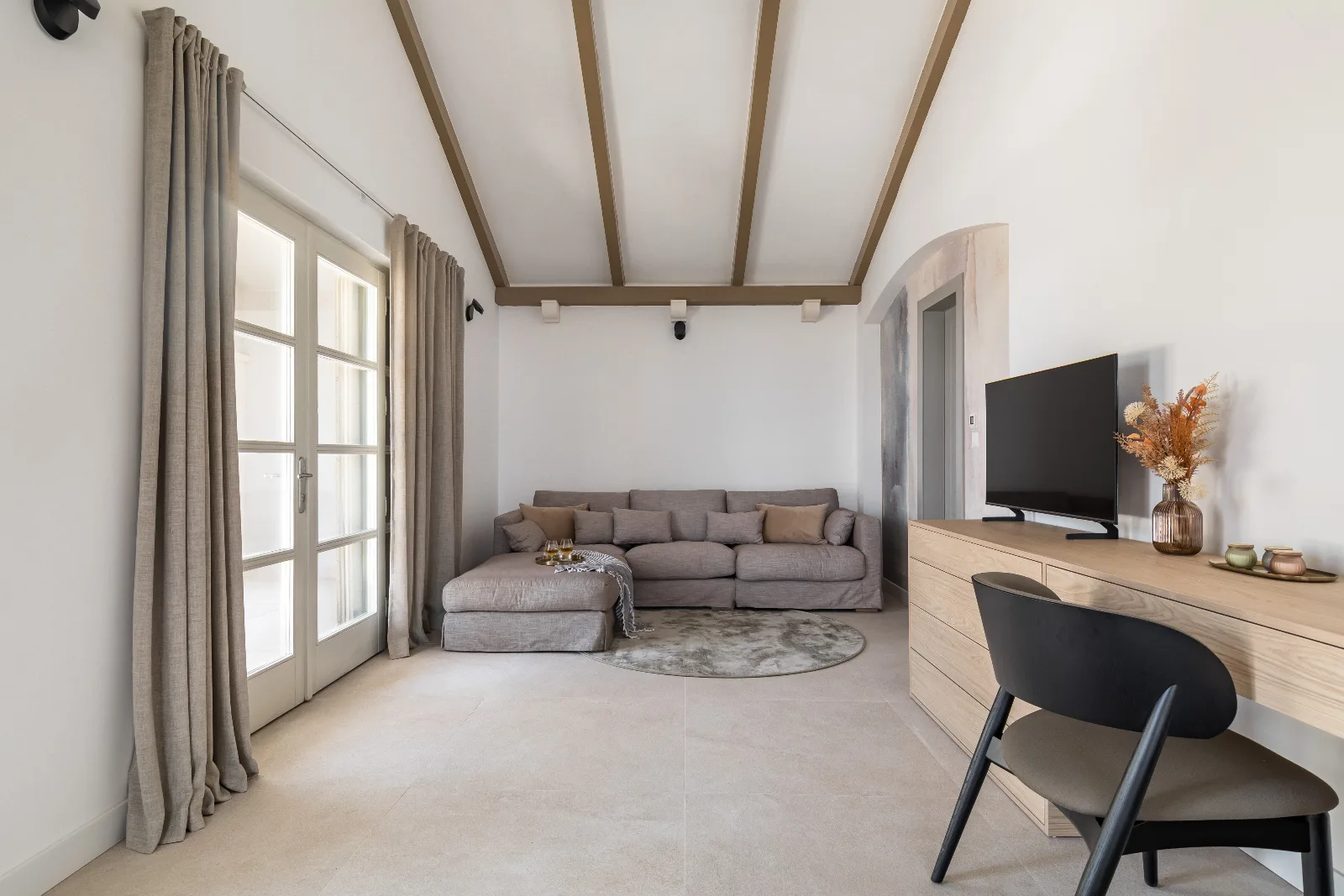 Living room with a taupe corner sofa, oak media cabinet and full-height linen curtains