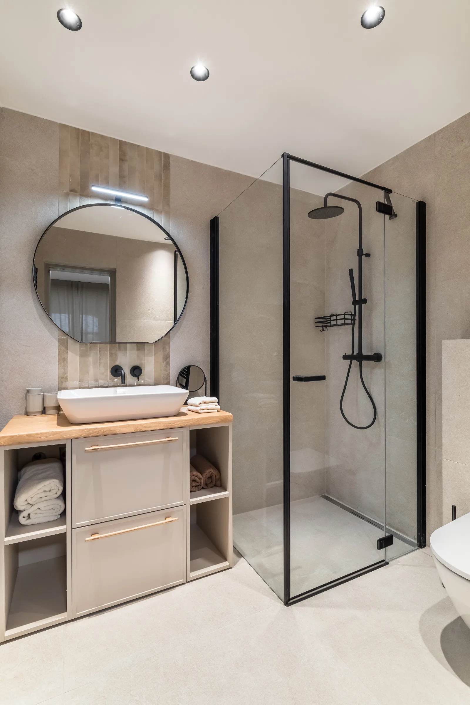 Bathroom with an oak vanity, round mirror and black-framed walk-in shower