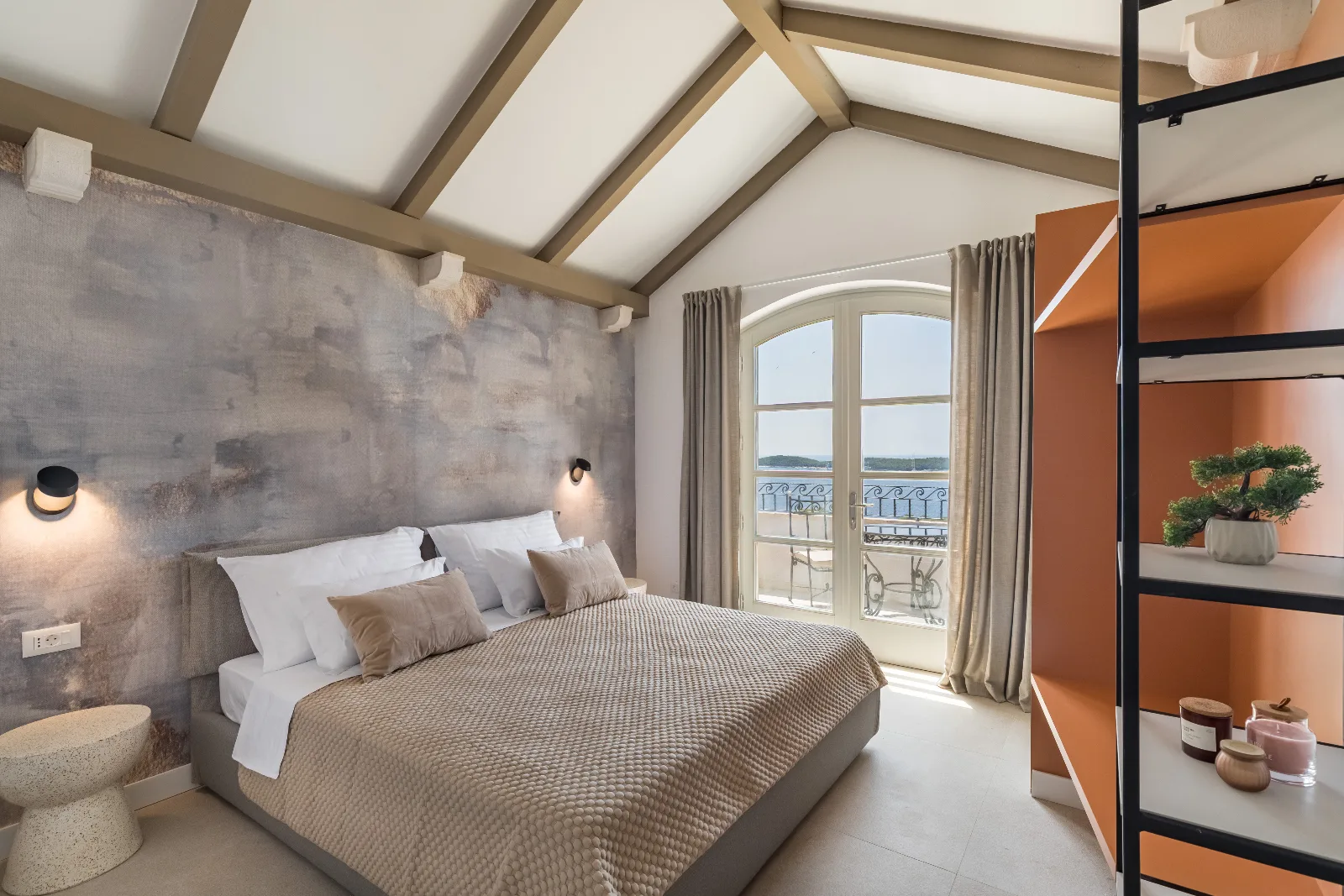 Bedroom with exposed roof beams, orange shelving and a balcony over the harbour