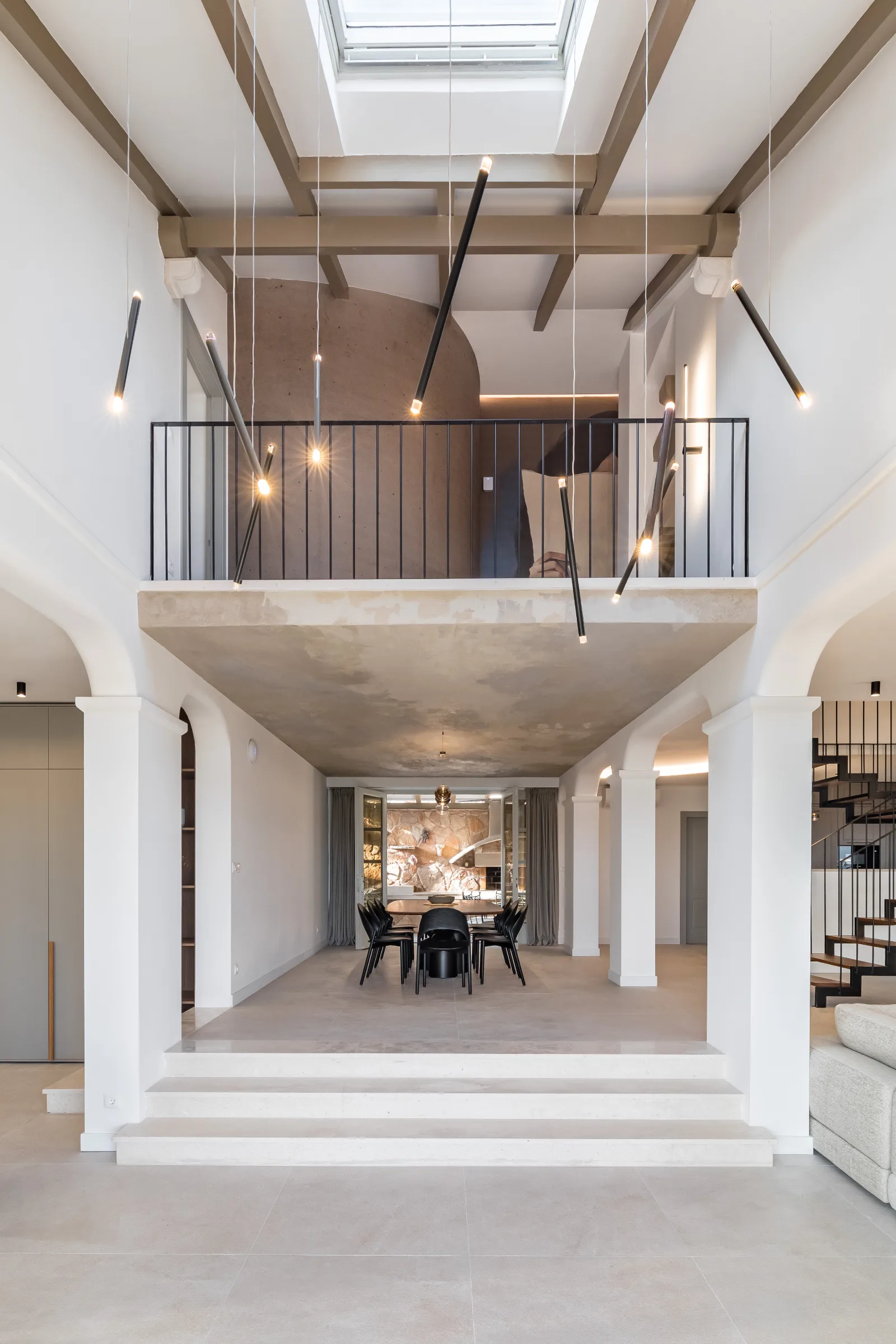 Double-height living hall with a mezzanine, skylit timber beams and a stone gallery front