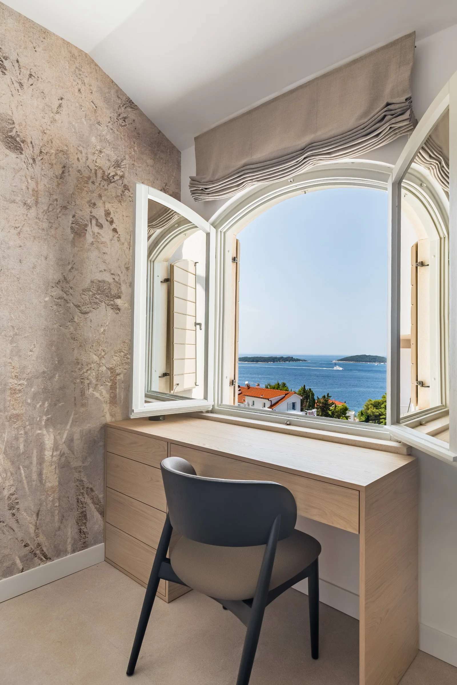 Built-in oak desk at an arched window opening to the sea