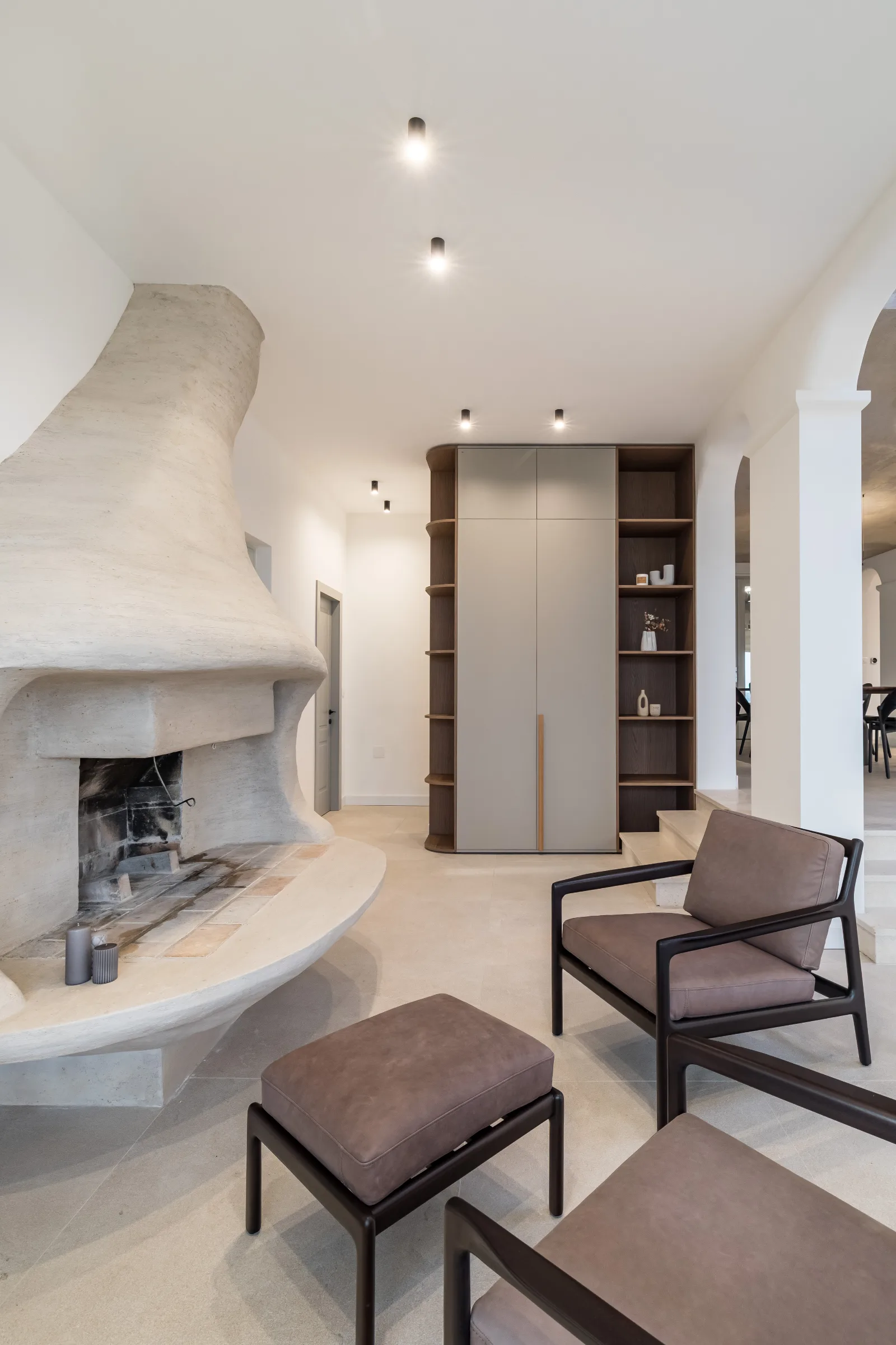 Lounge with a sculptural stone fireplace, walnut cabinet wall and leather armchairs