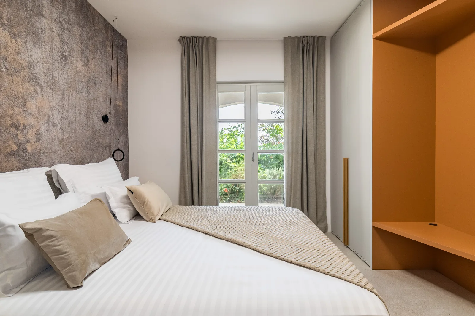 Guest bedroom in soft neutrals with an orange wardrobe niche and a garden view