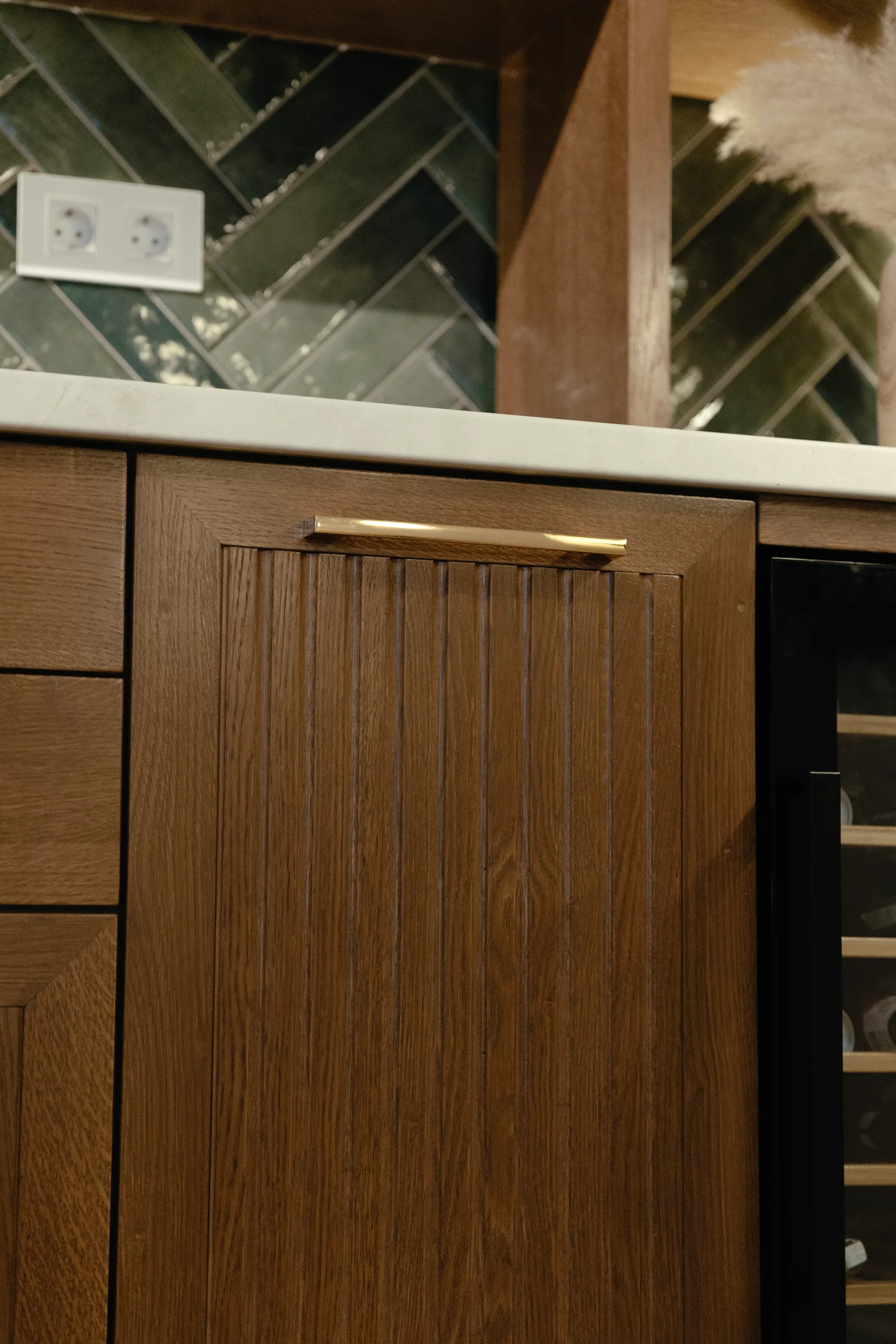 Fluted oak cabinet door with a brass pull against green herringbone tiles
