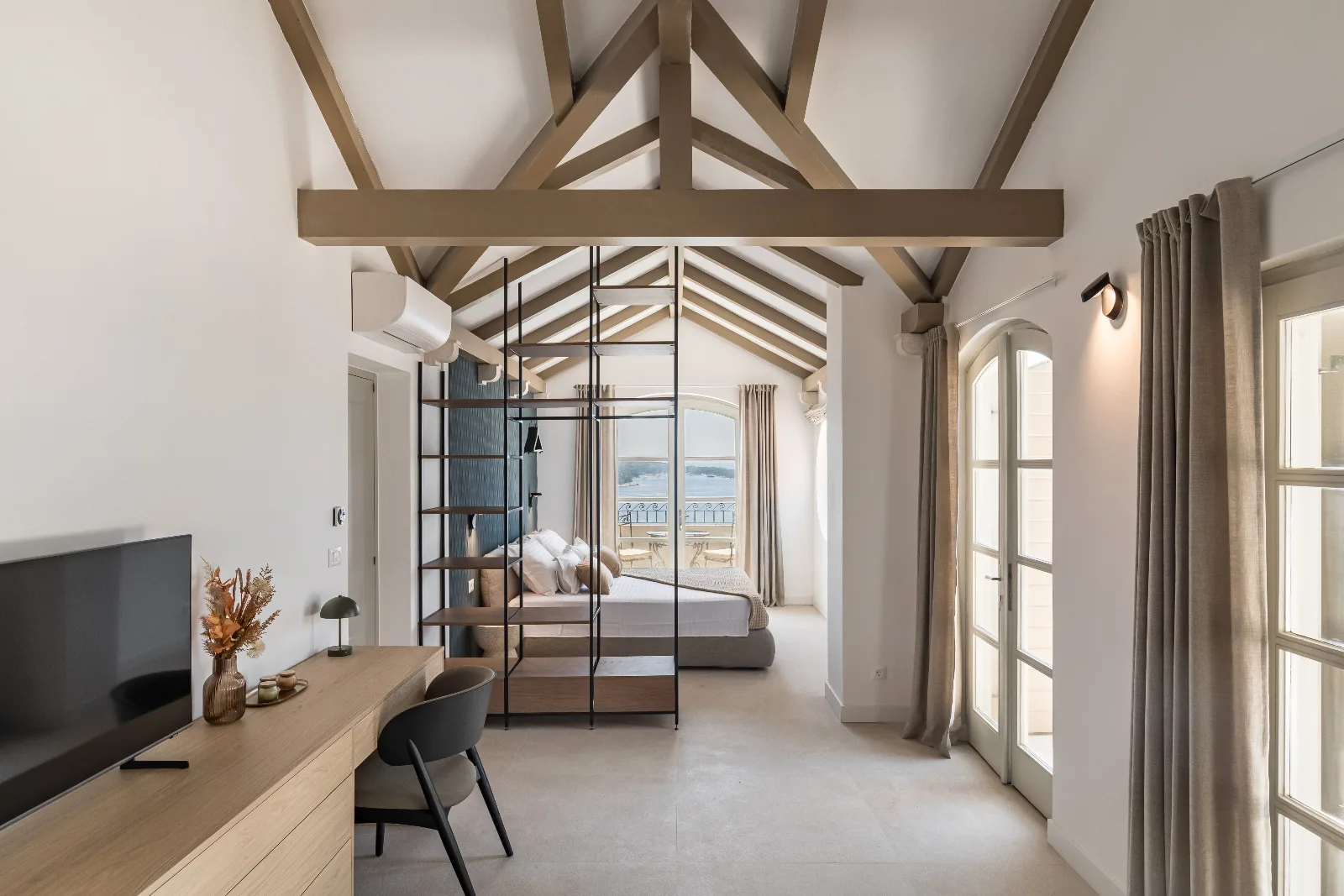 Attic suite under exposed trusses with a glass partition and a built-in oak media desk