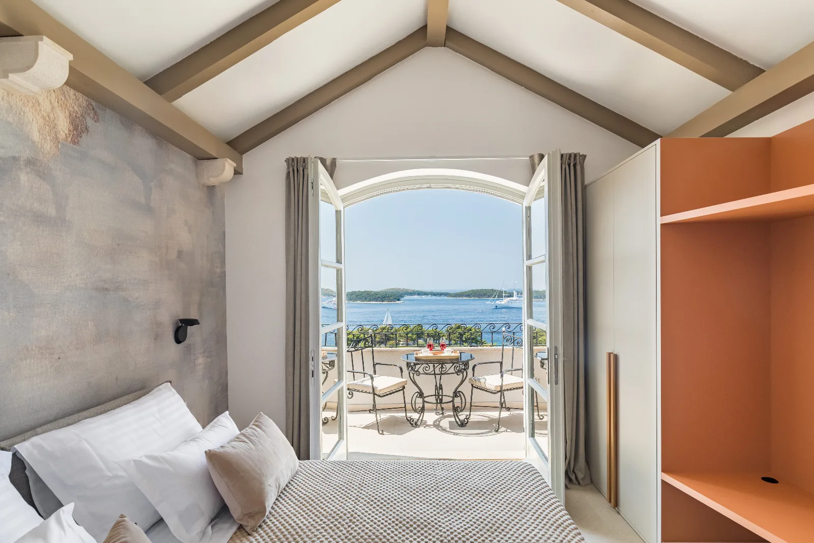 Bedroom under timber beams opening onto a terrace above the bay
